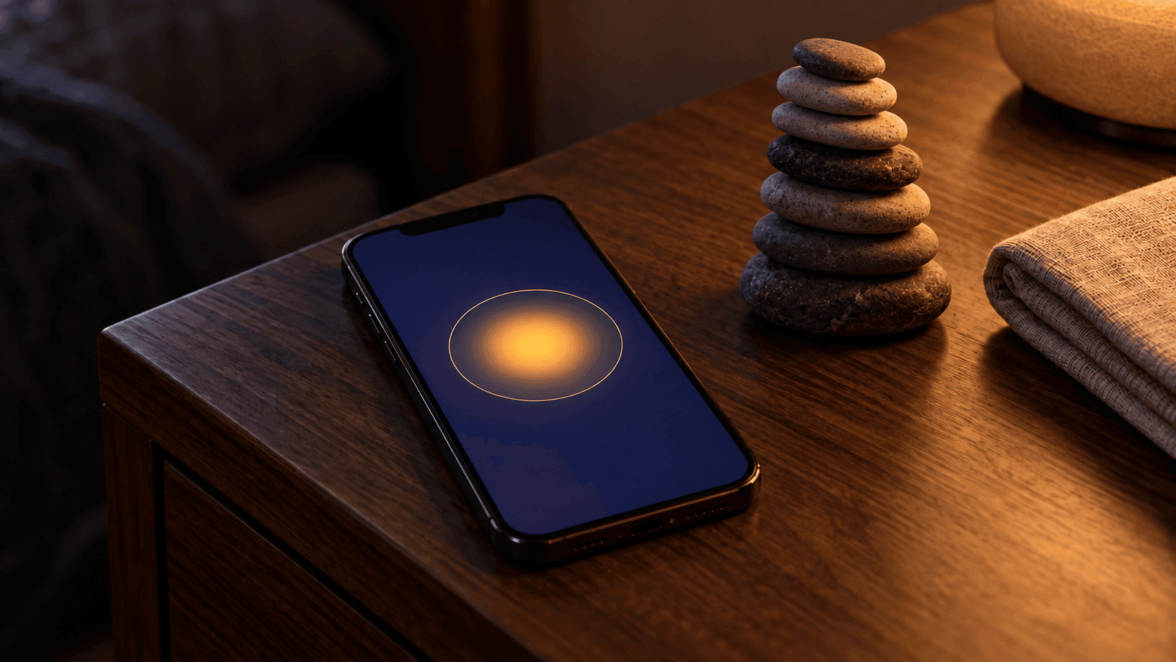 Chambre le soir, iPhone sur une table de chevet en noyer affichant l’app Arnasea avec son halo de souffle ambré sur fond indigo, pile de sept galets à côté.